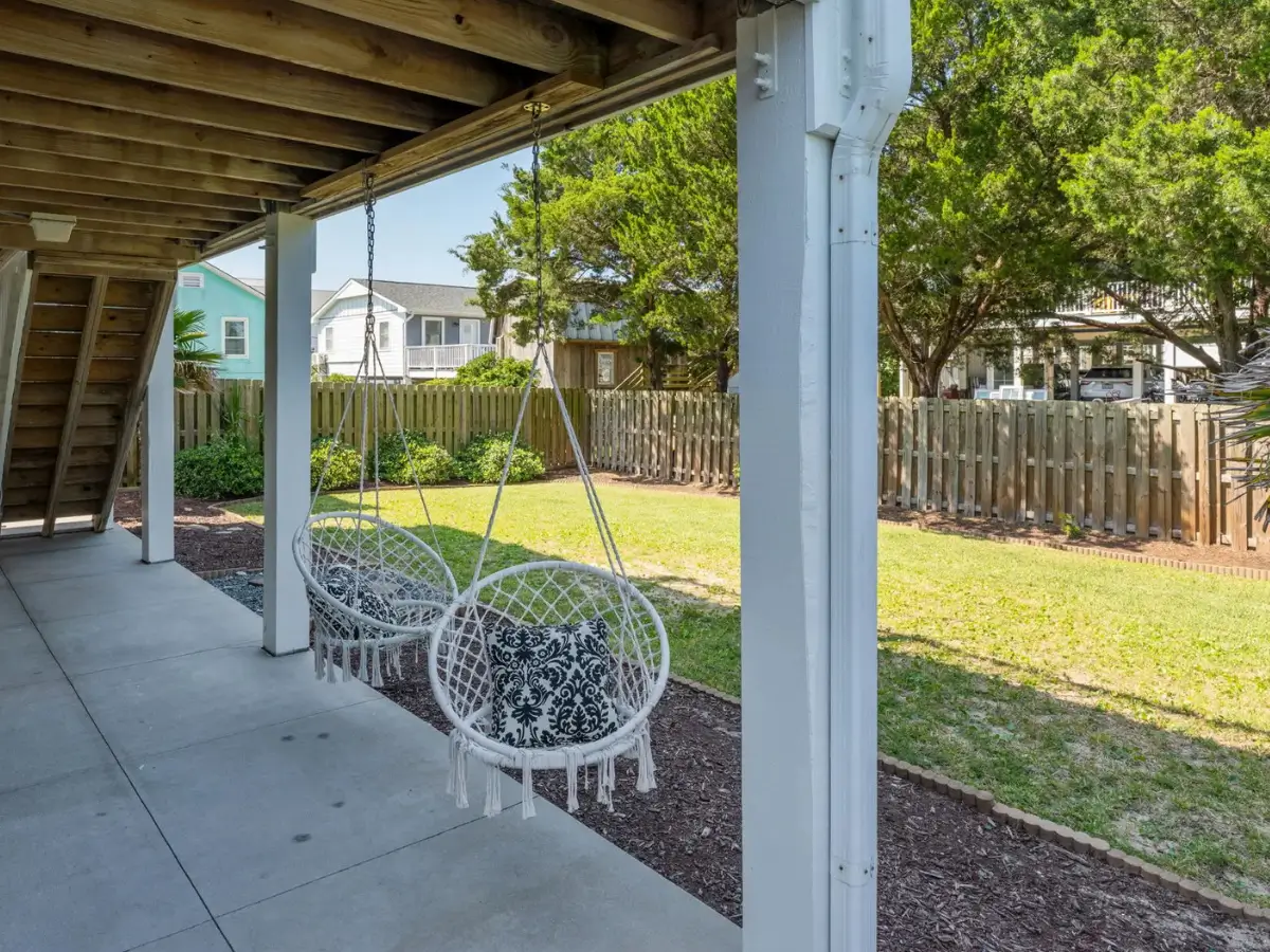 Covered ground-level patio with hanging chairs overlooking the fenced backyard at Salty Dream vacation rental.