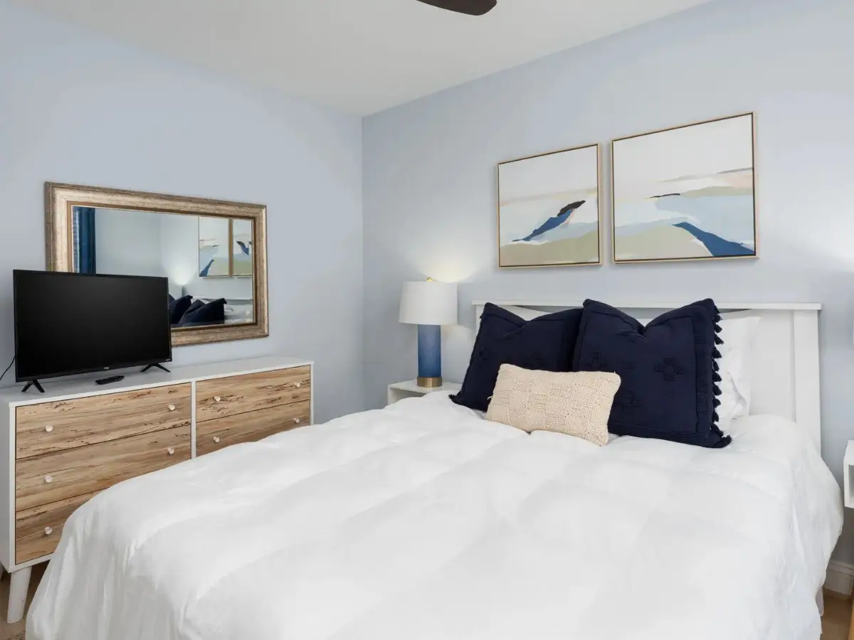 Comfortable guest bedroom with queen bed, coastal artwork, and dresser with TV.