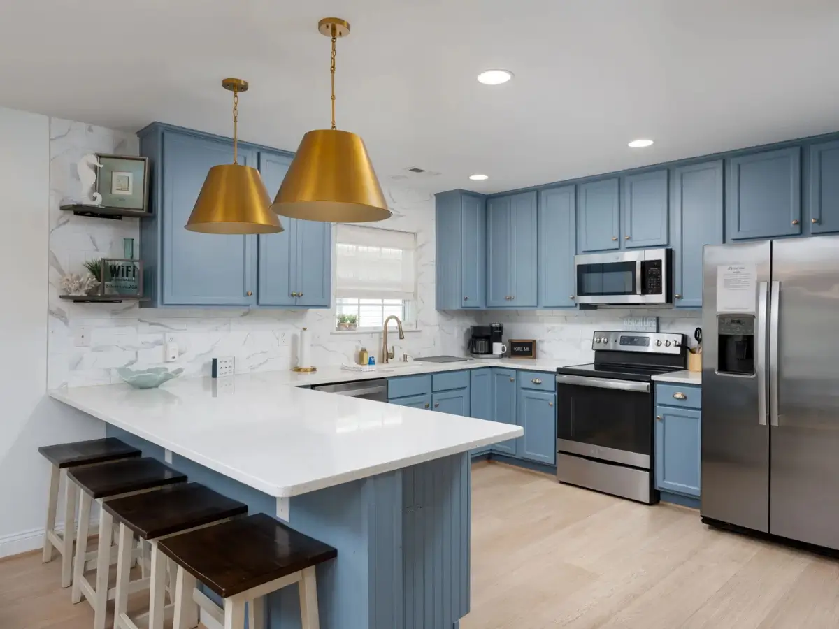 Modern coastal kitchen with blue cabinetry, large island, quartz countertops, and stainless steel appliances.