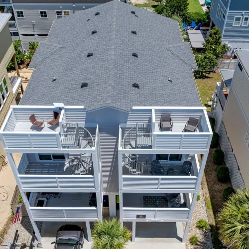 Exterior of A Sail Away vacation rental townhouse in Carolina Beach with covered parking, multiple balconies, and rooftop deck.